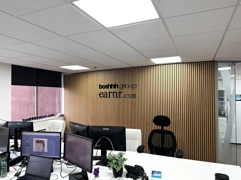 An image of the black acrylic Boshhh signage against a vertical wood wall in a meeting room.